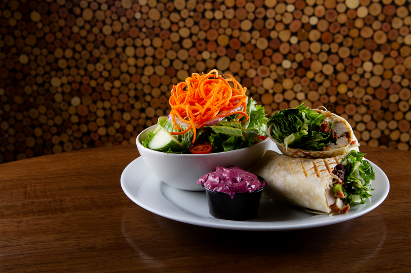 A chicken bacon caesar wrap cut in half with a bowl of salad and a cup of dipping sauce